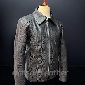 Może przedstawiać: Czarna skórzana kurtka z teksturowanym wzorem przypominającym skórę węża. Kurtka ma kołnierz, zamek błyskawiczny na całej długości i długie rękawy. Widoczny jest napis "Artisan Leather".