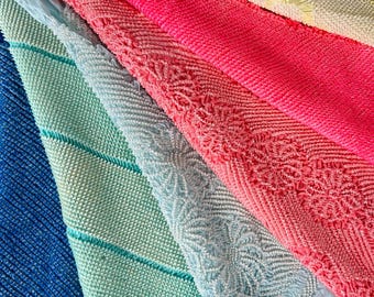 May include: A collection of colorful, textured fabrics in shades of blue, green, pink, and yellow. The textiles feature various patterns, including diagonal lines and floral designs. The fabrics are layered, creating a visually appealing display of color and texture.