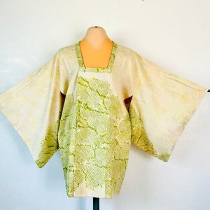 Puede incluir: Un kimono japonés tradicional con un patrón de piel de serpiente verde y blanco. El kimono está hecho de seda y tiene mangas anchas.