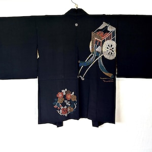 Pode incluir: Quimono preto com um design decorativo com um carro e bordados florais. O quimono tem mangas largas e está pendurado em um fundo branco. O design do carro inclui detalhes prateados e vermelhos.