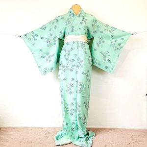 Könnte beinhalten: Ein mintgrüner Kimono mit einem weißen Obi-Gürtel. Der Kimono hat ein zartes Blumenmuster in Blau- und Grüntönen. Die Ärmel sind weit und fließend, und das Kleidungsstück wird auf einer Schaufensterpuppe präsentiert.