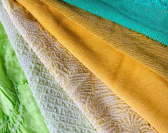 May include: Close-up of colorful fabric swatches in shades of green, white, and yellow. The textures vary from smooth to textured, with a crinkled effect on some. The fabrics are arranged diagonally, showcasing their different patterns and colors.