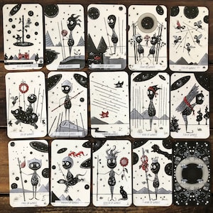 May include: A deck of tarot cards with black and white illustrations of stick figures with a starry night sky background. The cards feature the suit of wands.