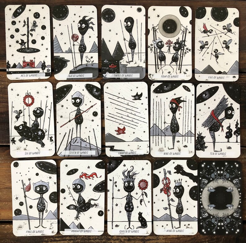 May include: A deck of tarot cards with black and white illustrations of stick figures with a starry night sky background. The cards feature the suit of wands.