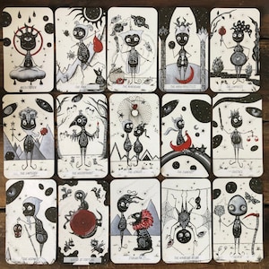 May include: A set of 22 tarot cards featuring black and white illustrations of whimsical characters with various symbols. The cards are printed on a white background with black borders.