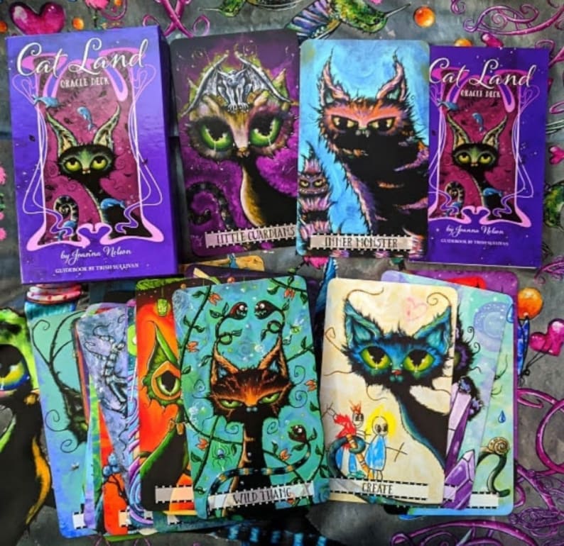May include: A set of Cat Land Oracle Deck cards featuring colorful illustrations of cats with whimsical designs. The cards include titles like "Inner Monster", "Wild Thang", and "Create".