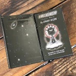 May include: A black hardcover book with a white illustration of a black cat on a cloud with a crescent moon and stars in the background. The book title is "Don't Worry, It's Just a Dream" by Joanna Hollen. The book cover is illustrated with a black cat with a white eye and a white crescent moon.