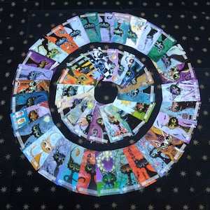 May include: A set of 32 colorful tarot cards featuring whimsical illustrations of cats with various expressions and poses. The cards are arranged in a circle on a black background with white stars.