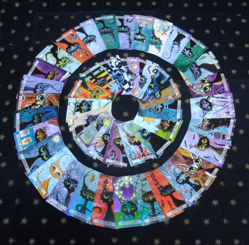 May include: A set of 32 colorful tarot cards featuring whimsical illustrations of cats with various expressions and poses. The cards are arranged in a circle on a black background with white stars.