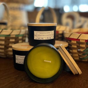 May include: Three black scented candles with wooden lids. The candles are in a variety of scents, including "Musk" and "Pine".