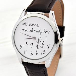 May include: A silver wristwatch with a black leather band. The watch face is white with black numbers and the text "who cares, I'm already late".