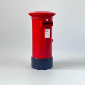 May include: A bright red, cylindrical mailbox with a black base. The mailbox has a slot for mail and a small sign with text. The top of the mailbox is rounded. The mailbox is a classic design.