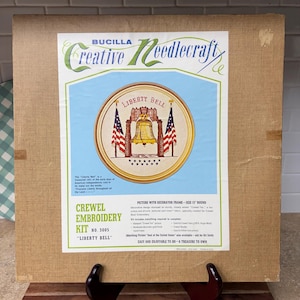May include: A Bucilla Creative Needlecraft crewel embroidery kit, number 3005, titled Liberty Bell. The packaging features a 15-inch round picture with a gold frame, displaying the Liberty Bell flanked by two American flags and stars.