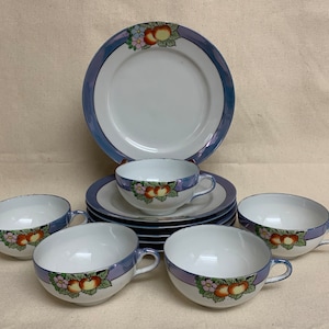 May include: A set of six vintage teacups and saucers with a blue and white floral design. The cups and saucers feature a delicate floral pattern with orange and yellow accents. The set includes a larger plate with a similar design.