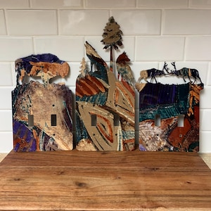 May include: Three decorative light switch covers with a nature theme. Each cover features a different animal silhouette: a bear, a wolf howling at the moon, and two deer. The covers have a colorful, abstract painted design.