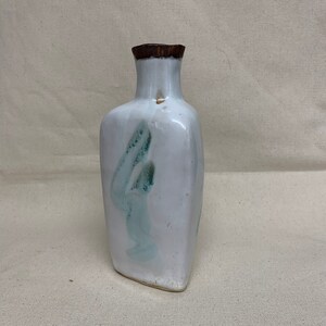 May include: A white ceramic vase with a brown rim and a light blue and green abstract design.