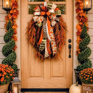 May include: A front door decorated with a large wreath featuring orange foliage and a multi-patterned bow with pumpkin, leopard, and checkered prints. A tan doormat with the word welcome in black script sits on a black and white checkered floor.