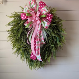 May include: A green wreath with a pink and white floral ribbon bow. The bow has pink polka dots and pink stripes.