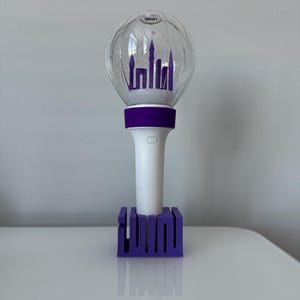 May include: A purple light stick with a clear plastic globe containing a silhouette of a castle. The light stick is on a purple base with the word "IU" written on it.