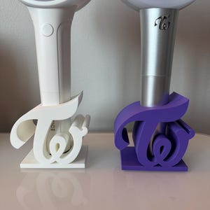May include: Two white and silver light-up concert lights with the word "Twice" in a stylized font on the side. The lights are in white and purple stands shaped like the word "Twice".