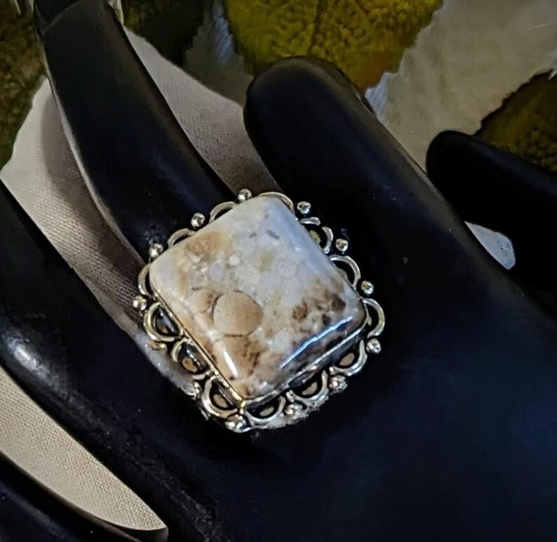 Pode incluir: Anel de prata com uma pedra quadrada de cor clara com padr&otilde;es castanhos e bege. A pedra &eacute; colocada numa moldura de prata decorativa com uma borda ondulada. Um anel marcante, adequado para uso di&aacute;rio ou ocasi&otilde;es especiais.
