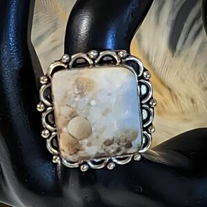 Pode incluir: Anel de prata com uma pedra retangular de cor clara. A pedra tem um padr&atilde;o salpicado de bege e castanho. A crava&ccedil;&atilde;o do anel &eacute; ornamentada, com uma borda ondulada e pequenas contas decorativas.
