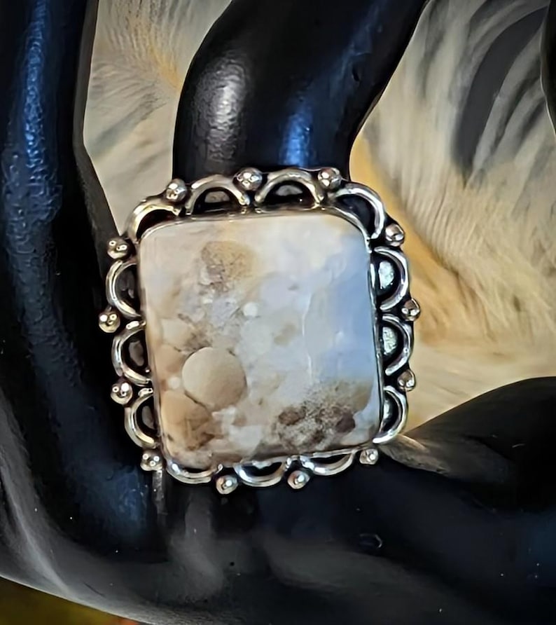 Pode incluir: Anel de prata com uma pedra retangular de cor clara. A pedra tem um padr&atilde;o salpicado de bege e castanho. A crava&ccedil;&atilde;o do anel &eacute; ornamentada, com uma borda ondulada e pequenas contas decorativas.