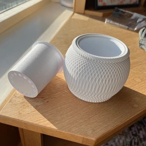 Op de afbeelding: Witte keramische plantenpot met een geometrisch patroon en een aparte witte plastic afvoertrechter.