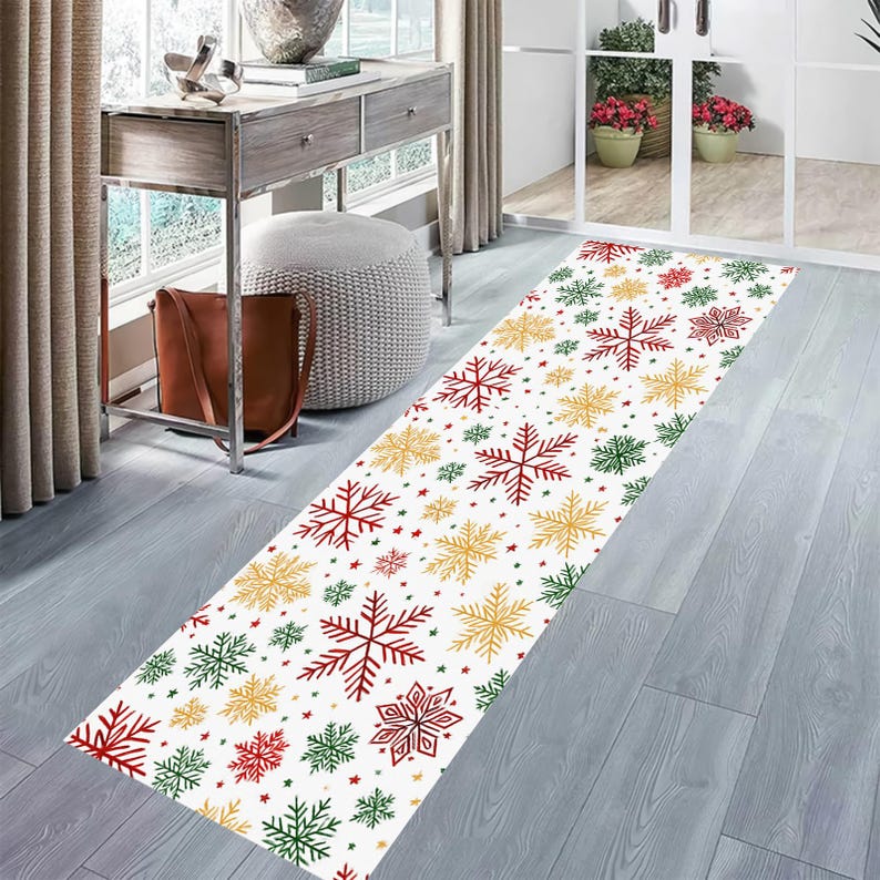 Op de afbeelding: Een witte loper met een herhalend patroon van rode, groene en gouden sneeuwvlokken en sterren. Het rechthoekige tapijt ligt op een lichtgrijze houten vloer. De loper is een decoratief item voor een hal of entree.