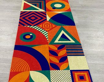 May include: A long, rectangular rug with a geometric pattern in shades of red, orange, yellow, green, blue, and white. The rug is made up of various shapes, including circles, squares, triangles, and rectangles.