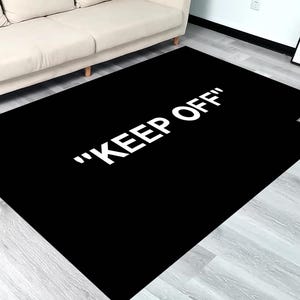 Puede incluir: Alfombra negra y blanca con el texto "KEEP OFF" en letras blancas. La alfombra est&aacute; sobre un suelo de madera clara.