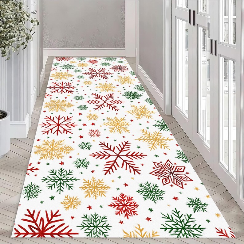 Op de afbeelding: Een witte loper met een herhalend patroon van rode, groene en gouden sneeuwvlokken en kleine sterren. De loper ligt in een gang met witte muren en een lichte houten vloer. Een feestelijke vakantiedecoratie.