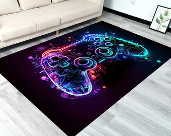 Puede incluir: Una alfombra rectangular que presenta un gráfico vibrante de colores neón de un mando de videojuegos. El diseño utiliza tonos brillantes de azul, morado y rojo sobre un fondo negro intenso, con salpicaduras y líneas abstractas alrededor del mando.