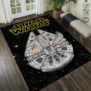 May include: A black and white Star Wars themed rug featuring a yellow "Star Wars" logo and a detailed image of the Millennium Falcon spaceship against a black background with white stars.