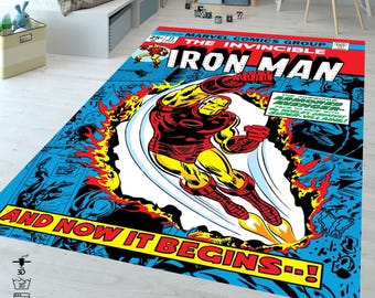 Puede incluir: Una alfombra rectangular con un diseño de portada de cómic de Iron Man en vuelo. La alfombra tiene un fondo azul con acentos rojos, amarillos y negros. El texto incluye "IRON MAN" y "AND NOW IT BEGINS--!".