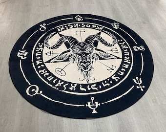 Op de afbeelding: Rond zwart-wit tapijt met een geitenkop- en pentagram-ontwerp. Het tapijt heeft een zwarte achtergrond met witte symbolen en tekst.