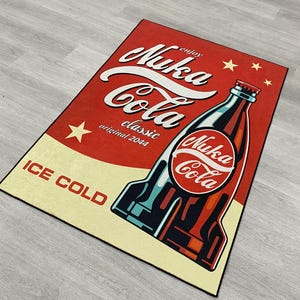 May include: A rectangular area rug featuring a vintage-style Nuka-Cola advertisement. The design includes a large red background, a stylized soda bottle, and the text Nuka-Cola, enjoy, classic, original 2044, and ICE COLD in bold lettering.