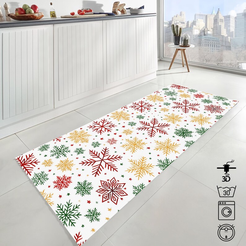 Op de afbeelding: Een rechthoekig wit keukenkleed met een sneeuwvlokkenpatroon in rood, groen en goud. De sneeuwvlokken vari&euml;ren in grootte en zijn verspreid over het kleed. Kleine sterren zijn ook aanwezig.