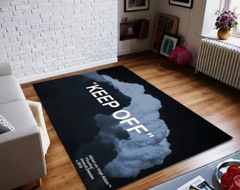 May include: A rectangular black rug with a cloud design and the words "KEEP OFF" in white. The rug also features text indicating the designer and manufacturer. The rug is placed on a wooden floor.