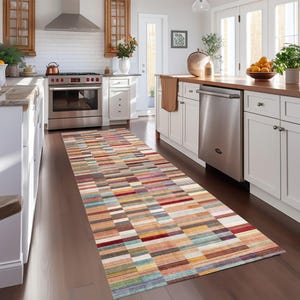 May include: A long, rectangular rug with a colorful, geometric pattern of horizontal stripes in shades of orange, red, blue, and brown. The rug is placed on a dark wood floor in a kitchen setting.