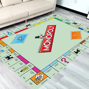 May include: A green and red Monopoly game board rug with the word "MONOPOLY" printed in large red letters. The rug features a variety of squares with different colors, numbers, and symbols.