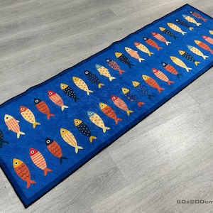 Pode incluir: Tapete retangular azul com um padrão repetido de peixes coloridos. Os peixes são de várias cores, incluindo amarelo, laranja, vermelho e preto. O tapete mede 60 cm x 200 cm.
