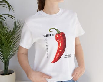 Op de afbeelding: Wit T-shirt met een grote, felrode chilipeper afbeelding en het woord "CHILLI" erboven. Het ontwerp bevat Chinese karakters en een groene steel. Een casual T-shirt voor dagelijks gebruik.