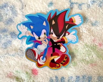 Pode incluir: Um adesivo recortado apresentando o personagem ouriço azul Sonic e o personagem ouriço preto e vermelho Shadow de costas um para o outro. Ambos usam luvas brancas e sapatos vermelhos e brancos sobre um fundo vibrante rosa e laranja.