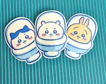 Op de afbeelding: Drie cartoon dieren stickers op een blauwe achtergrond. Elke sticker heeft een ander dier in een toiletpot. De dieren zijn een kat, een beer en een konijn. De kat draagt een blauwe strik. De beer is wit met zwarte ogen. Het konijn is geel met bruine oren.