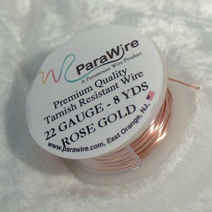 May include: A spool of rose gold wire from ParaWire. The label reads "Premium Quality Tarnish Resistant Wire 22 GAUGE - 8 YDS ROSE GOLD." The wire is a light copper color and is wound around a clear plastic spool.