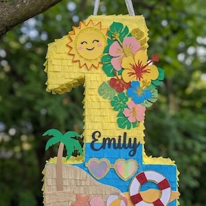 Puede incluir: Una piñata con forma de número uno decorada con flecos amarillos, un sol sonriente, flores tropicales y hojas verdes. La sección inferior presenta una escena de playa con una palmera, gafas de sol en forma de corazón, un salvavidas y el nombre Emily.