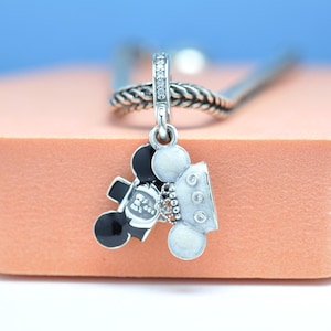 May include: A silver charm featuring a Mickey Mouse design. One side is black with a white face, the other is white with three small clear stones. The charm is suspended from a silver chain.