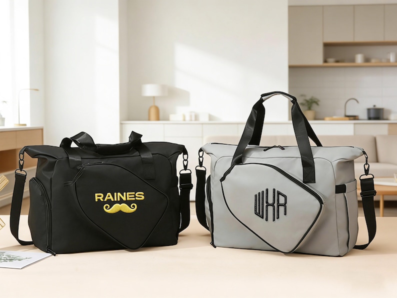 K&ouml;nnte beinhalten: Zwei Reisetaschen, eine schwarze und eine graue, stehen nebeneinander. Die schwarze Tasche hat "RAINES" und einen gelben Schnurrbart. Die graue Tasche zeigt "WXR" in Schwarz. Beide Taschen haben schwarze Griffe und Schultergurte.