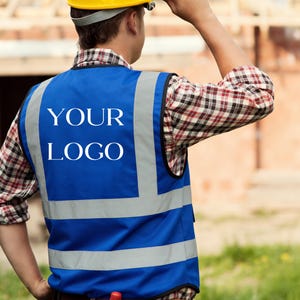 May include: A blue high-visibility safety vest featuring silver reflective strips and the text YOUR LOGO printed in white on the back. The vest is worn over a plaid long-sleeve shirt, with a yellow hard hat visible at the top of the frame.